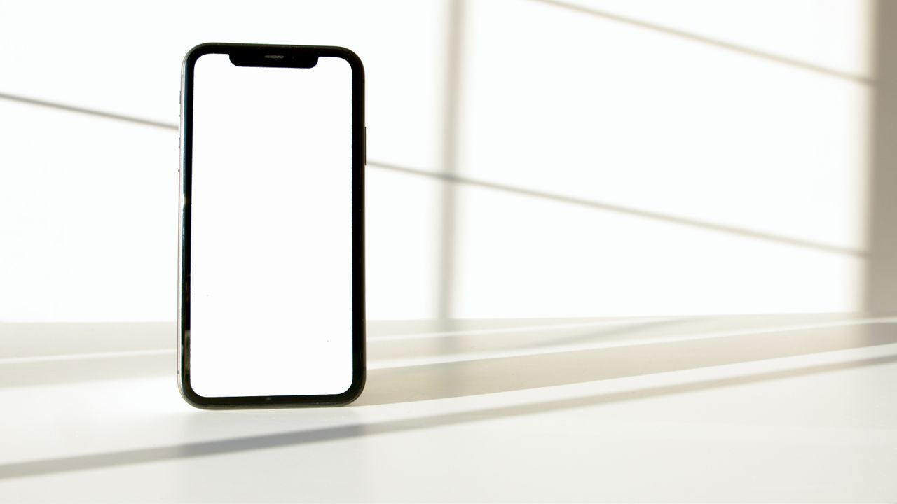 A sleek smartphone displayed on a white surface with dramatic light and shadow contrast.